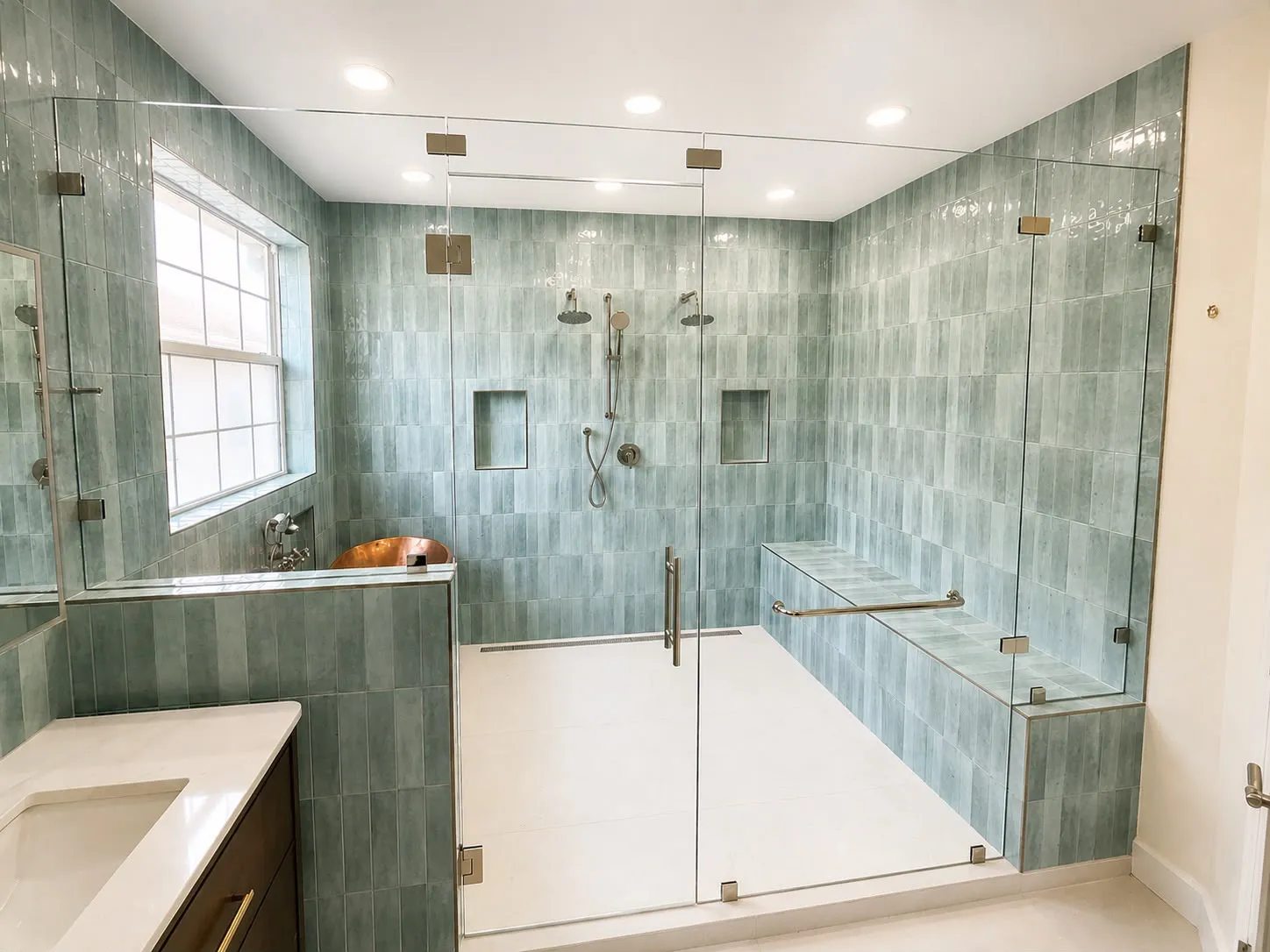 Wet room in sea-green tile with twin rain heads, a bench and a copper soaking tub