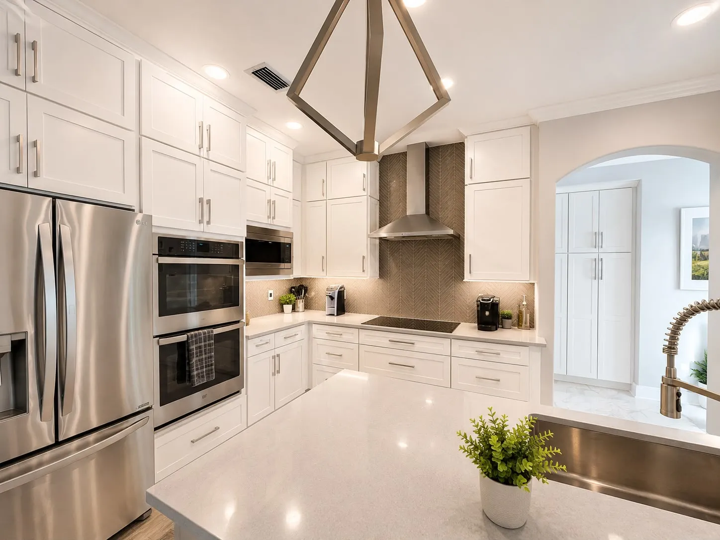 White shaker kitchen with a stainless chimney hood over a herringbone tile feature wall