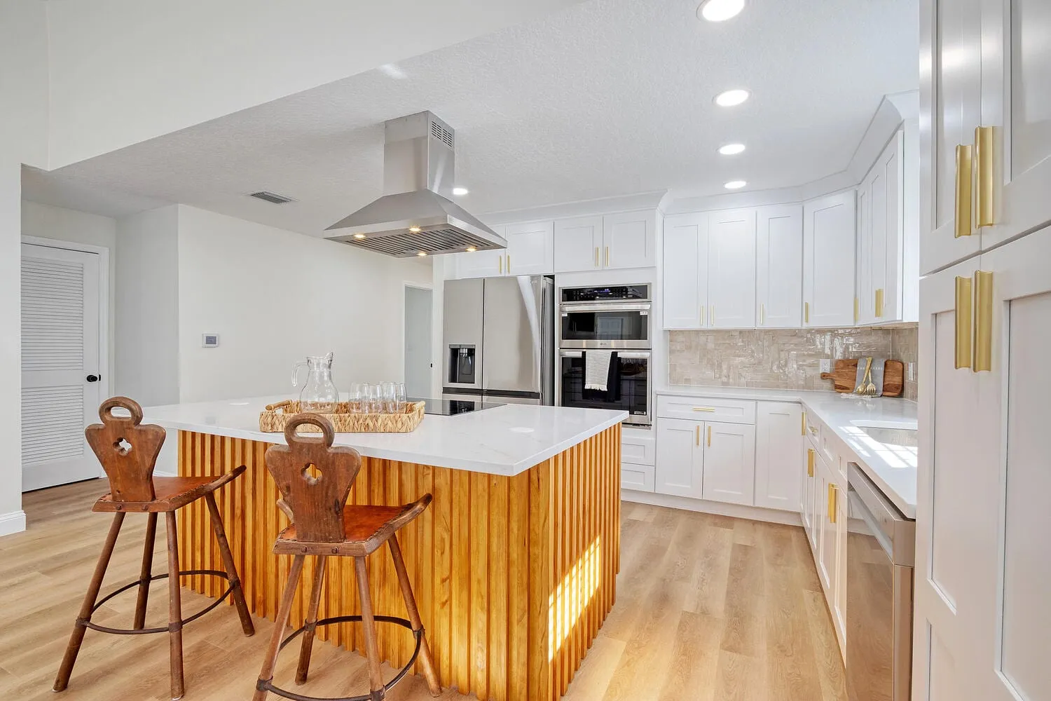 Renovated kitchen with a quartz island, vented hood and white shaker cabinetry